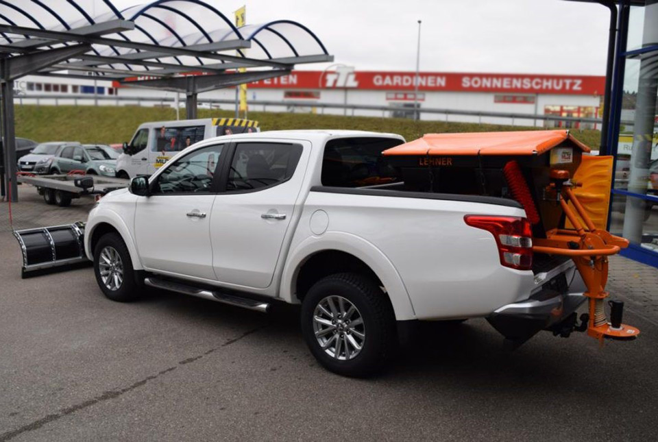 Weißer Pickup mit orangefarbener Schneeräumschaufel auf der Ladefläche, bereit für den Winterdienst.