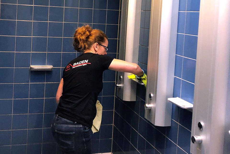 Frau reinigt Duschen in einem Schwimmbad.