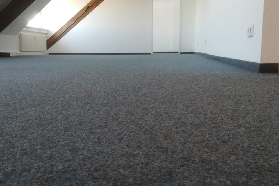 Bodenansicht eines sauberen, grauen Teppichs in einem hellen Raum mit schrägen Wänden.