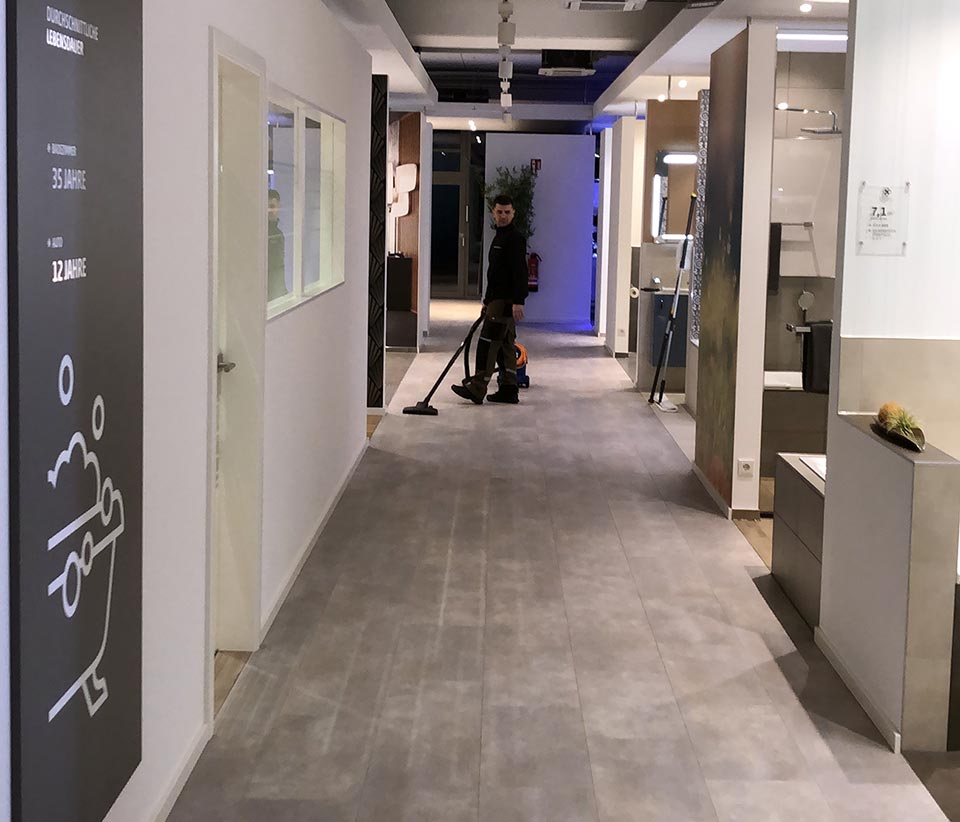 Ein Mitarbeiter reinigt den Ausstellungsraum mit einem Staubsauger. Der Raum zeigt moderne Badezimmer- und Fliesendesigns.