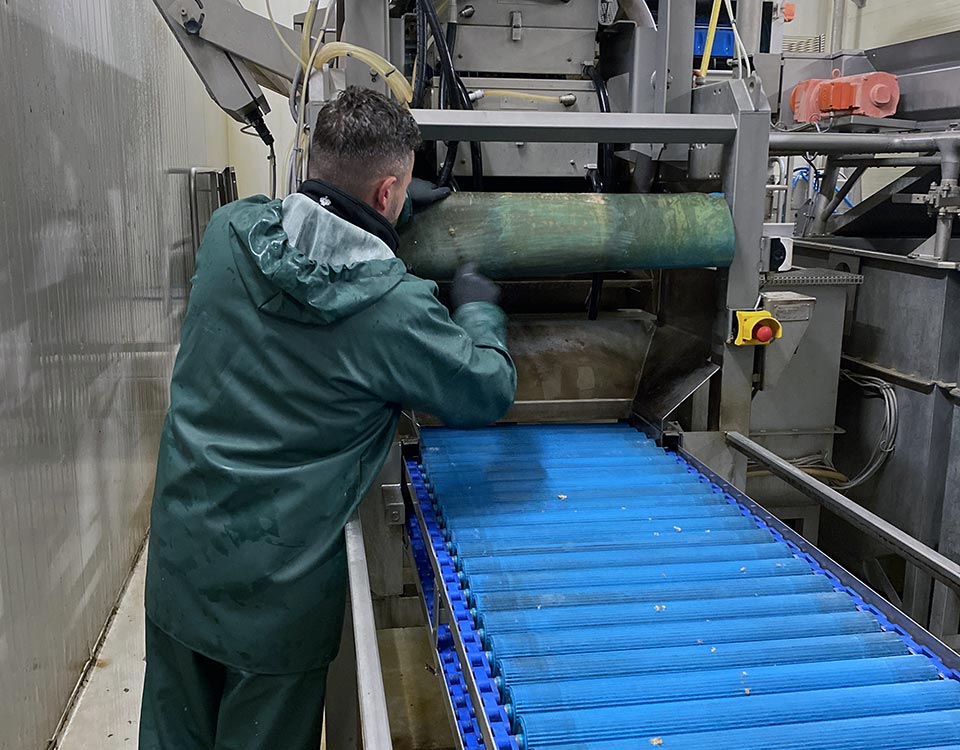 Ein Arbeiter in grüner Schutzkleidung reinigt eine Maschine an einem blauen Förderband.