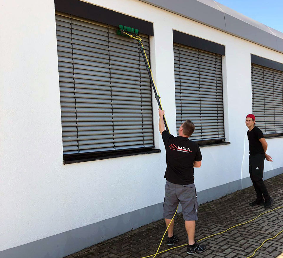 Zwei Personen reinigen Jalousien an einem Gebäude.